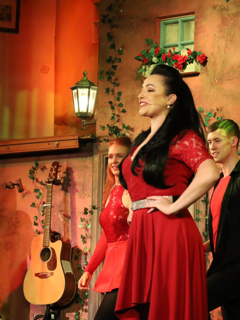 Performers in red outfits dancing on a stage with a rustic backdrop.