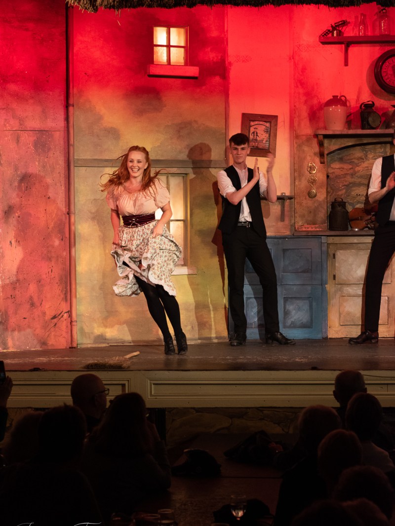 Dancers performing on stage with a colorful backdrop and audience in shadow.