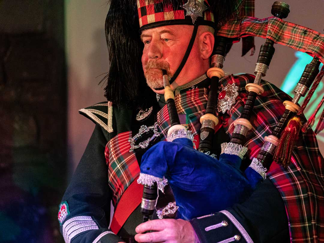 Man in traditional Scottish attire playing bagpipes.