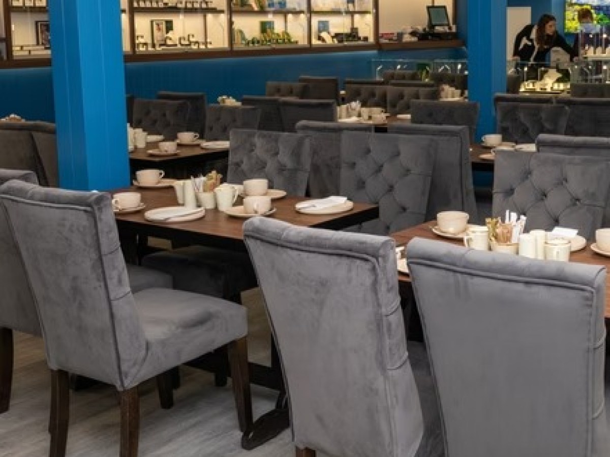 Empty restaurant with gray chairs and set tables, blue walls in background.