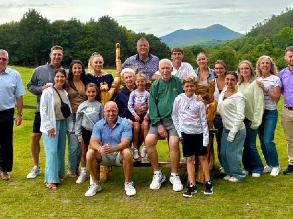 Group photo of people outdoors on a grassy field with mountains in the background.